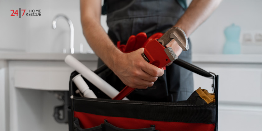 My Pipe Is Clogged – What Should I Do? Technician holding red pipe wrench standing by sink with plumbing tools