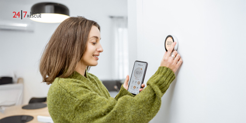 Hive vs Nest Thermostat: Best Smart Choice 2026 Woman in green sweater synchronizing a wireless thermostat with her smartphone