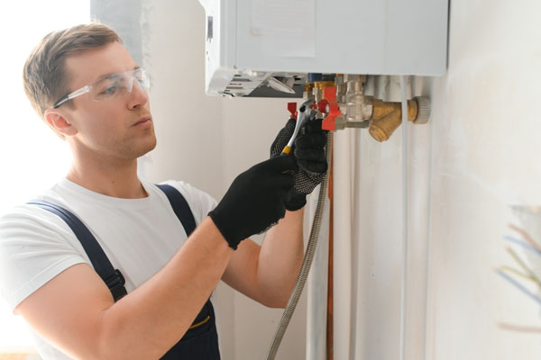 Engineer wearing safety goggles and gloves adjusting boiler valves and pipework