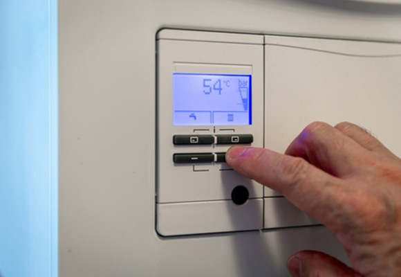 Hand adjusting temperature controls on a boiler display panel