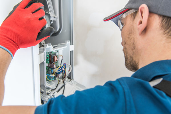 Engineer wearing safety glasses and a red glove inspecting the internal circuit board of a boiler