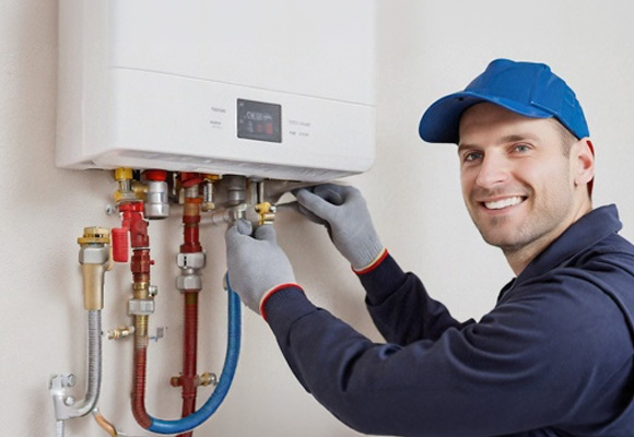 Engineer in navy uniform and blue cap installing a wall-mounted combi boiler