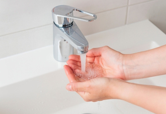 Hands washing under running warm water from a bathroom tap