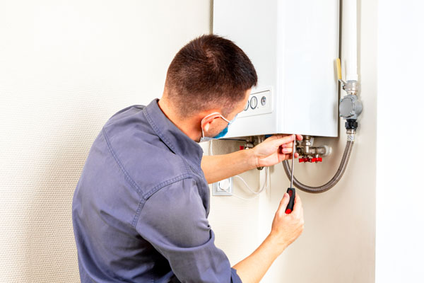 Engineer wearing a face mask using a screwdriver to service a wall-mounted boiler